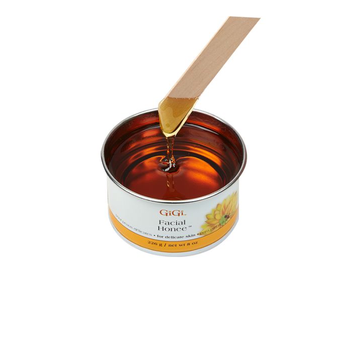 A small amount of GiGi Facial Honee Soft Wax on the applicator running down to its open can showcasing its texture and color